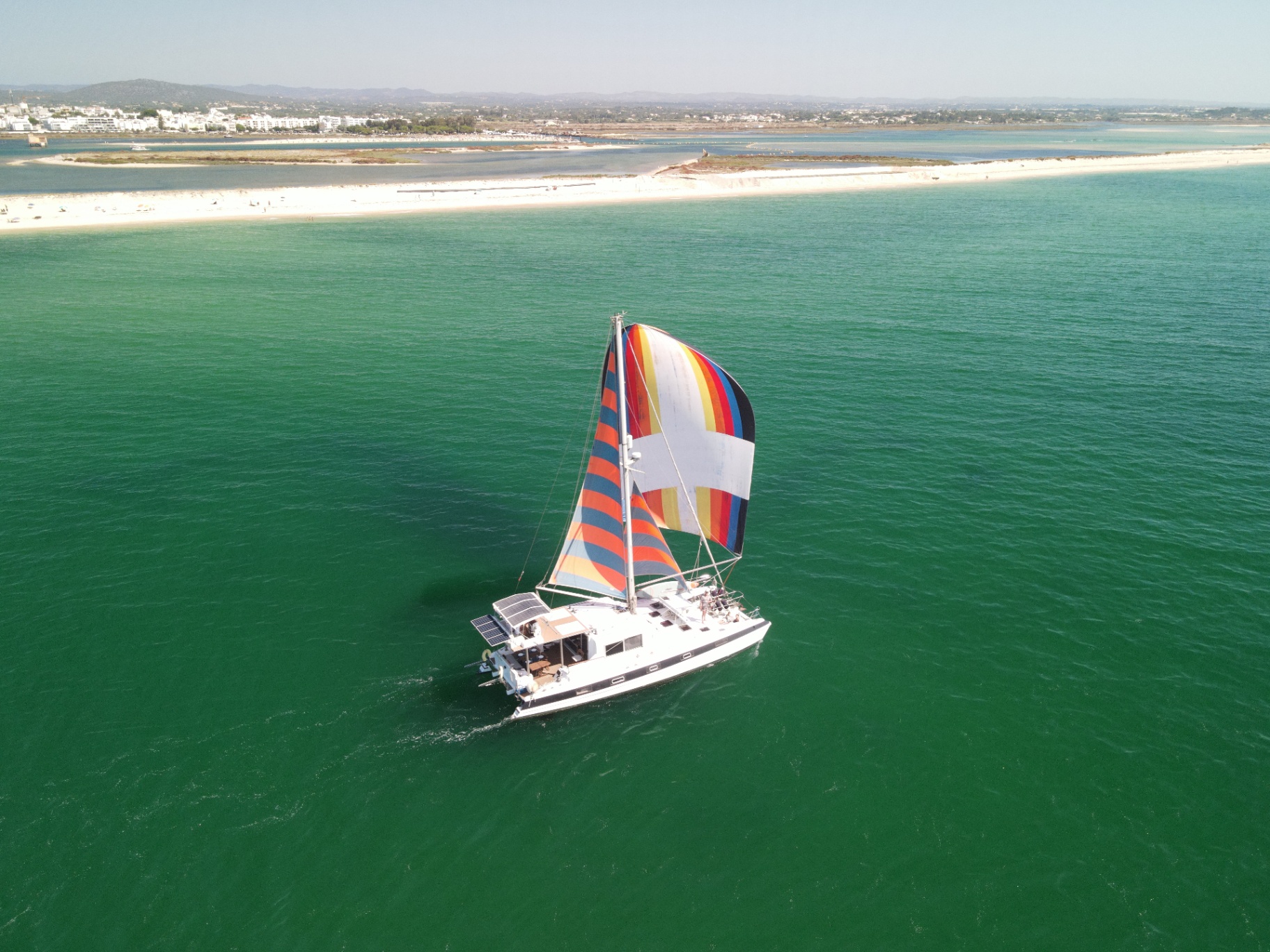 Blue Lagoon catamaran sailing with colourful spinnaker near the shore